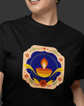 Person wearing a black t-shirt with a colorful Diwali-themed design featuring a lamp and flowers.